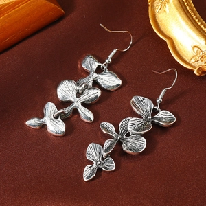 Detail van vintage zilveren oorbellen met drielaagse orchideeblaadjes kwastjes op donkere stof
