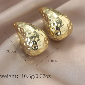 Detalle de pendientes de gota dorados con textura martillada y dimensiones de 3,0 cm x 1,8 cm