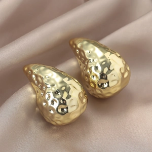 Pendientes retro dorados en forma de gota con textura martillada sobre seda