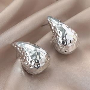 Detalle de pendientes de gota de plata martillada sobre seda color champán