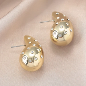 Detalle de pendientes de gota dorados con circonitas blancas sobre raso color champán