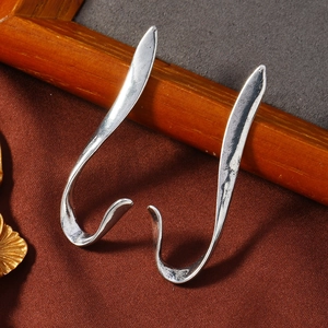 Detalle de pendientes colgantes plateados asimétricos con textura vintage mate y líneas