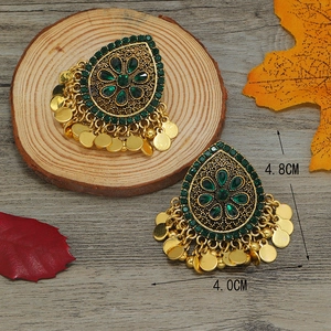 Primer plano de pendientes étnicos retro con piedras verdes y borlas de color dorado