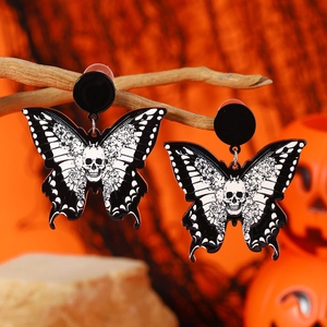 Halloween butterfly skull earrings hanging on dry branch with orange pumpkin background
