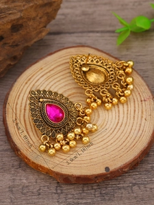 Detalle de pendientes étnicos dorados con piedra rosa en forma de gota sobre madera