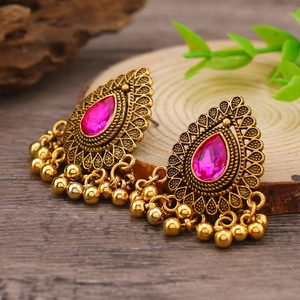 Primer plano de pendientes étnicos vintage con pedrería rosa y cuentas metálicas
