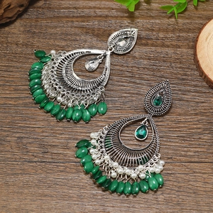 Detalle de pendientes bohemios vintage con cuentas verdes y perlas blancas en madera