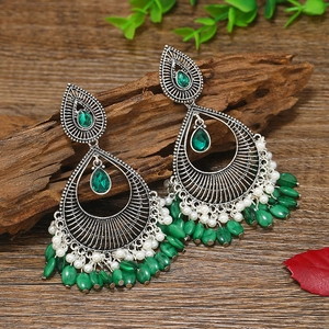 Detalle de pendientes étnicos boho con piedras verdes y perlas sobre madera rústica