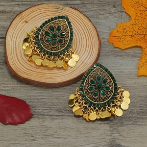 Detalle de pendientes étnicos dorados con pétalos verdes, pedrería y borlas de metal