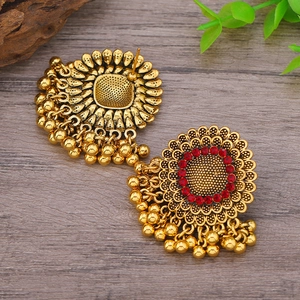 Detalle de pendientes vintage de flor dorada con pedrería roja sobre fondo de madera