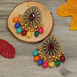 Detalle macro de pendientes étnicos dorados con gemas rojas y borlas de cuentas de colores
