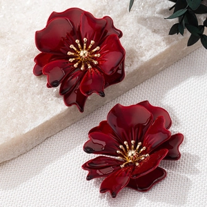 Elegant deep red enamel flower earrings with golden core on marble and woven background