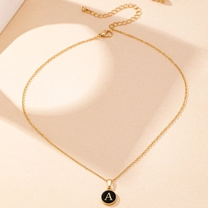 Detail of golden letter A necklace with black enamel pendant and lobster clasp closure