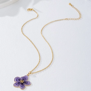 Collier avec pendentif fleur en émail violet et pétales dorés sur fond de pierre blanche