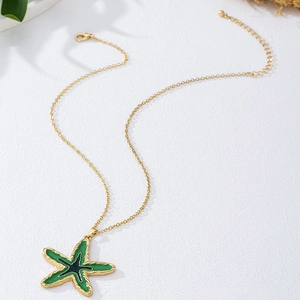 Detailopname van een gouden zeester hanger met groen emaille en een karabijnsluiting