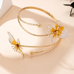 Dettaglio del bracciale a spirale dorato con ciondoli a forma di fiore sfumati bianco e giallo