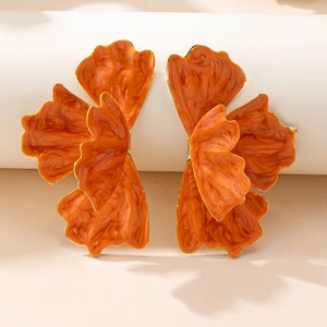 Macro shot of large vibrant orange flower earrings with layered petals on white stand