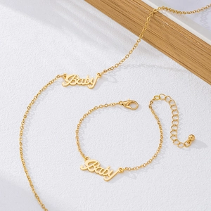 Elegant gold baby initial necklace and bracelet set on a textured surface