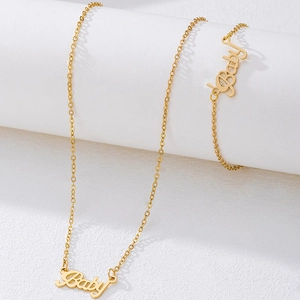 Detail of gold baby letter necklace and bracelet set draped on a white display stand