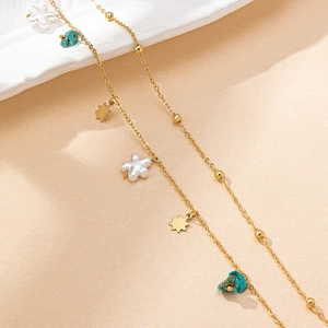 Golden star and pearl body chain with turquoise pendants on a sandy beach aesthetic background