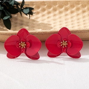 Nahaufnahme leuchtend roter Orchideen-Ohrringe mit goldenen Details auf Keramikteller