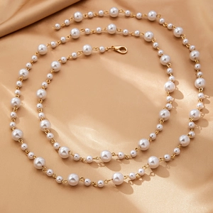 Détail d'une chaîne de corps en perles blanches sur satin champagne avec fermoir doré