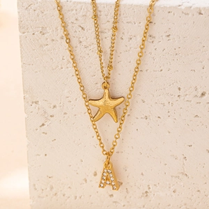 Dettaglio macro della collana doppia dorata con stella marina e lettera A con strass
