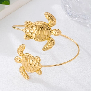 Bracciale rigido aperto dorato con tartarughe marine dettagliate su uno sfondo bianco estetico