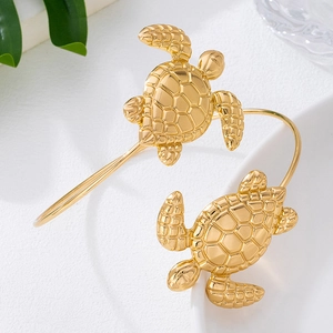 Bracciale rigido dorato con tartarughe marine e motivi geometrici su sfondo bianco