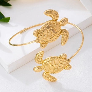 Dettaglio del bracciale rigido dorato con tartarughe su pietra bianca e foglie