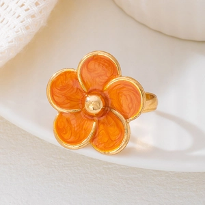 Détail macro d'une bague fleur dorée avec émail orange marbré sur une assiette en céramique