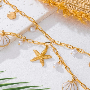 Detail of gold ocean-themed waist chain with starfish, shells, and pearls on white stone
