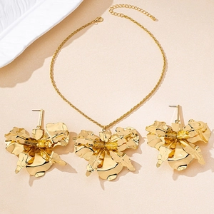 Detail view of a gold-finish orchid flower jewelry set on a textured beige backdrop