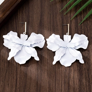 Macro detail of matte white blooming orchid earrings with golden studs on wooden surface