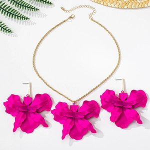 Flat lay of pink orchid necklace and earrings set with straw hat and fern decor
