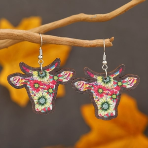 Detail of cow head earrings with colorful floral prints hanging on a natural wooden branch