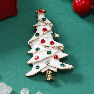 Close-up of a white enamel Christmas tree brooch with colorful rhinestones on green background