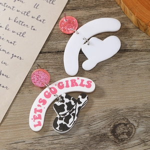 Detail of western earrings featuring cow print hat and Let's Go Girls text on wood surface
