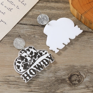 Detail of acrylic cowboy hat earrings with cow print and engraved HOWDY lettering