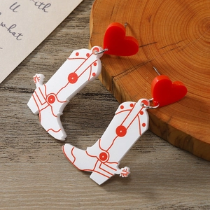 Macro detail of acrylic western cowboy boot and red heart earrings on a wooden base