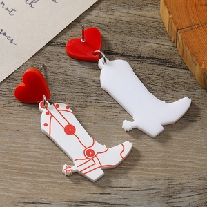 Detail of red heart acrylic earrings featuring western cowboy boot charms on wood background