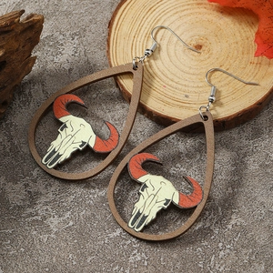 Macro detail of teardrop wooden earrings featuring a bohemian cow skull cutout design