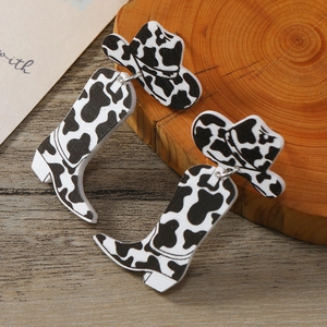Cow print acrylic cowboy hat and boot earrings on a vintage wooden background