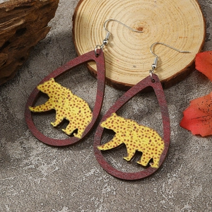 Detail view of teardrop wooden earrings with leopard pattern and natural fall leaf background