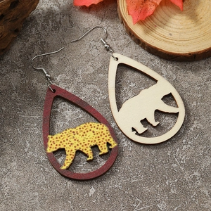 Close-up of wooden teardrop earrings with cutout bear design on a textured stone surface