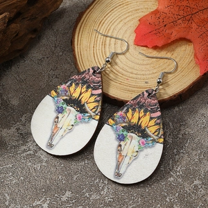 Makroaufnahme von Boho-Ohrringen mit Stierschädel und Sonnenblume auf rustikalem Holz