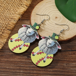 Detailed close-up of sheep earrings with green hats and baseball patterns on wood