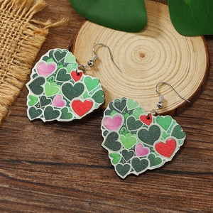 Dettaglio degli orecchini a cuore in legno con motivi verdi e rossi su una base rustica