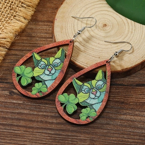Detailed close-up of teardrop wooden earrings with cat and clover art on rustic wood
