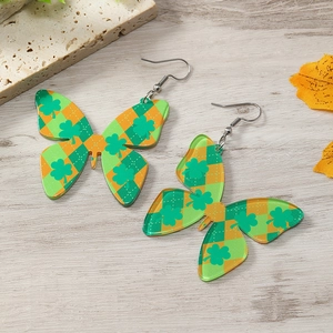 Detalle de pendientes de mariposa con trébol de San Patricio y diseño de cuadros